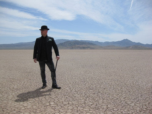 Vreny posing with cane and bowler hat in a scorching desert