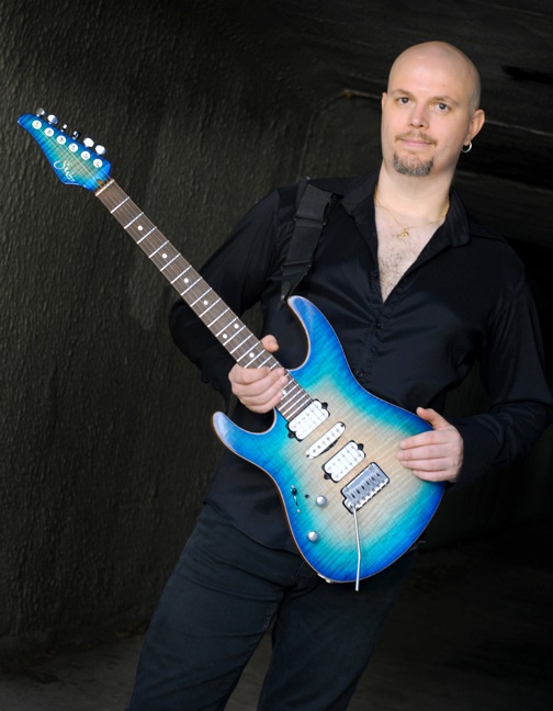 Head shot business photo of Vreny posing with his Suhr Modern