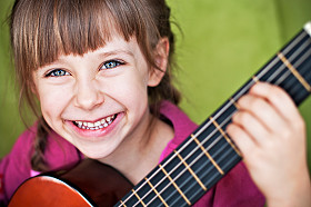 a stock photo of a laughing girl playing guitar