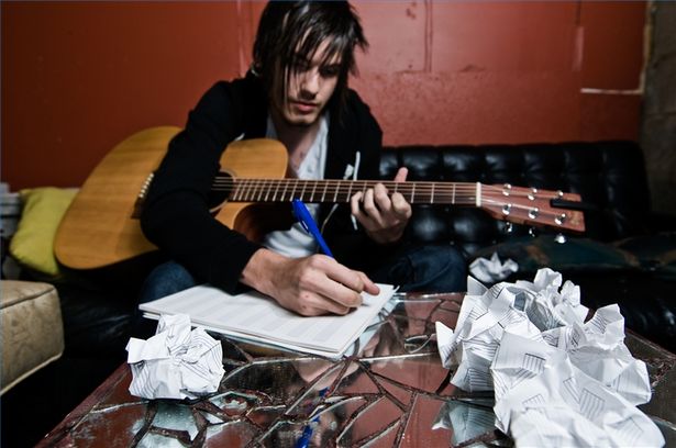 stock photo of a singer songwriter writing music on acoustic guitar