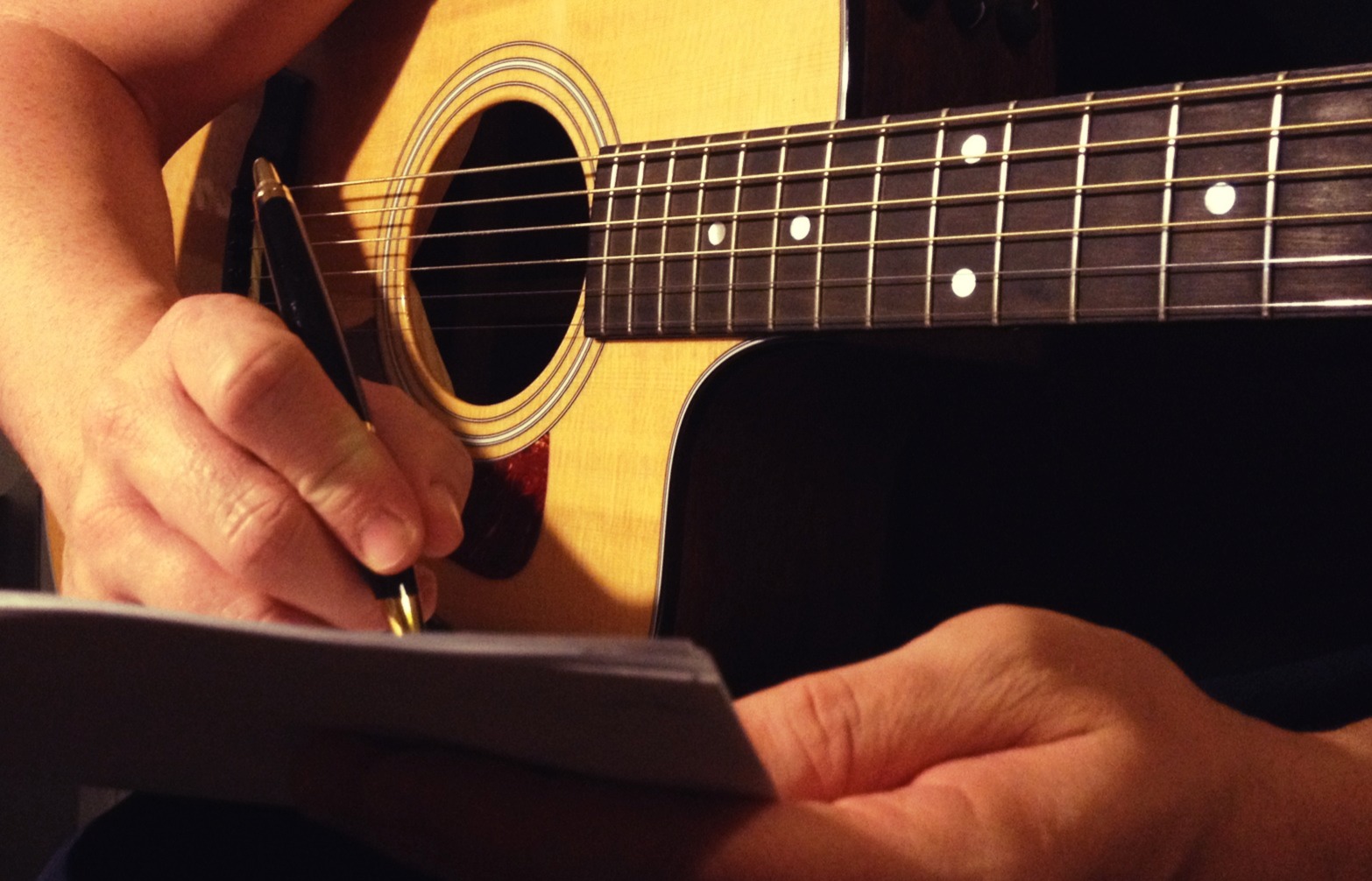 Stock photo of someone writing songs on an acoustic guitar