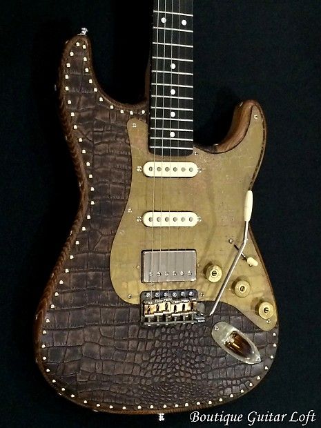 A snake skin clad Strat with metal rivets along the edge. Gold colored pick guard. 