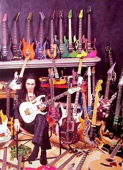 A picture of Steve Vai sitting surrounded by a vast guitar collection